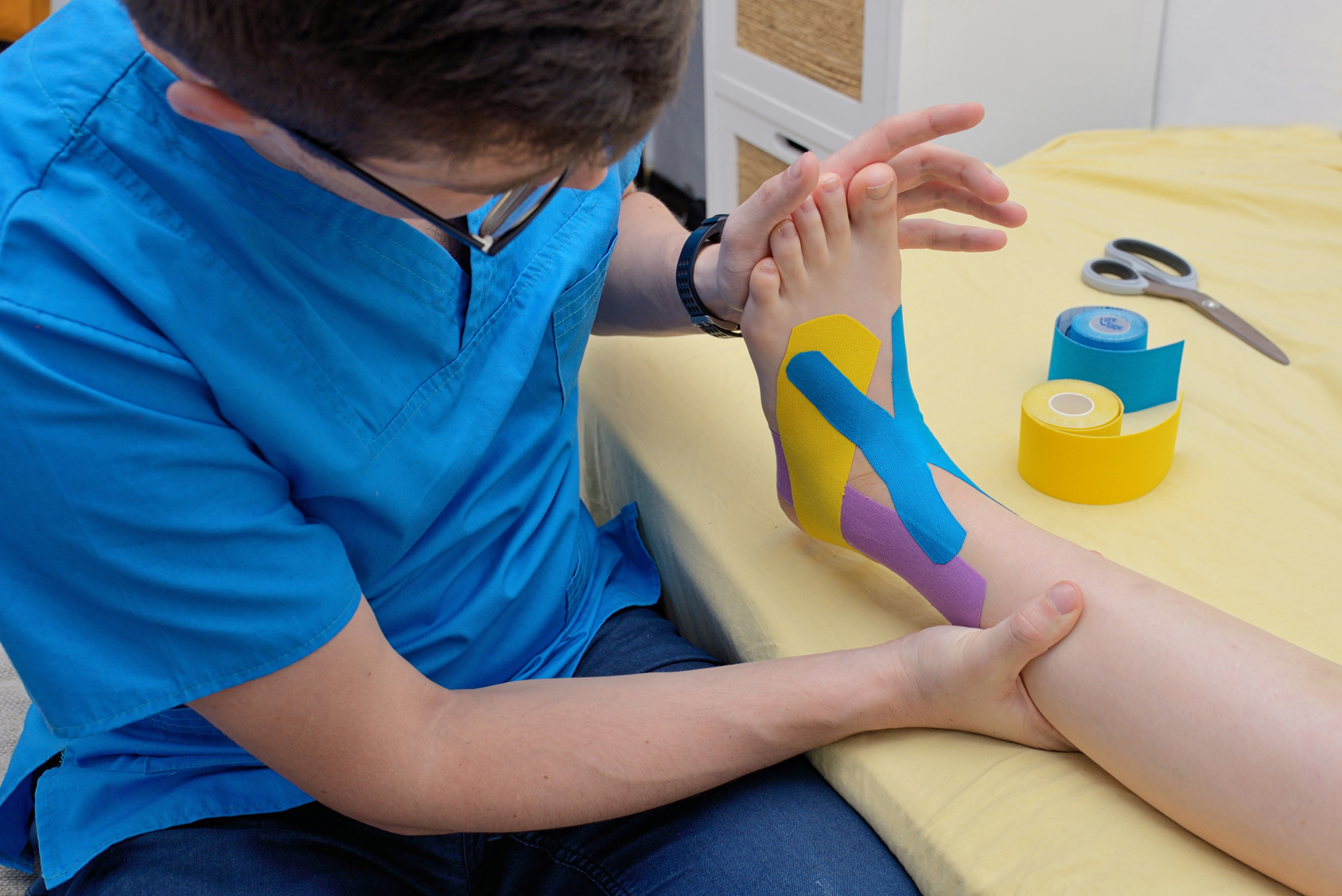 Physiotherapeut legt elastische Tapes am Fuß und Unterschenkel an